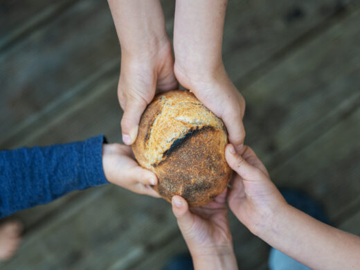 Hands of a family holding bread bun in a conceptual image of poverty and hunger.